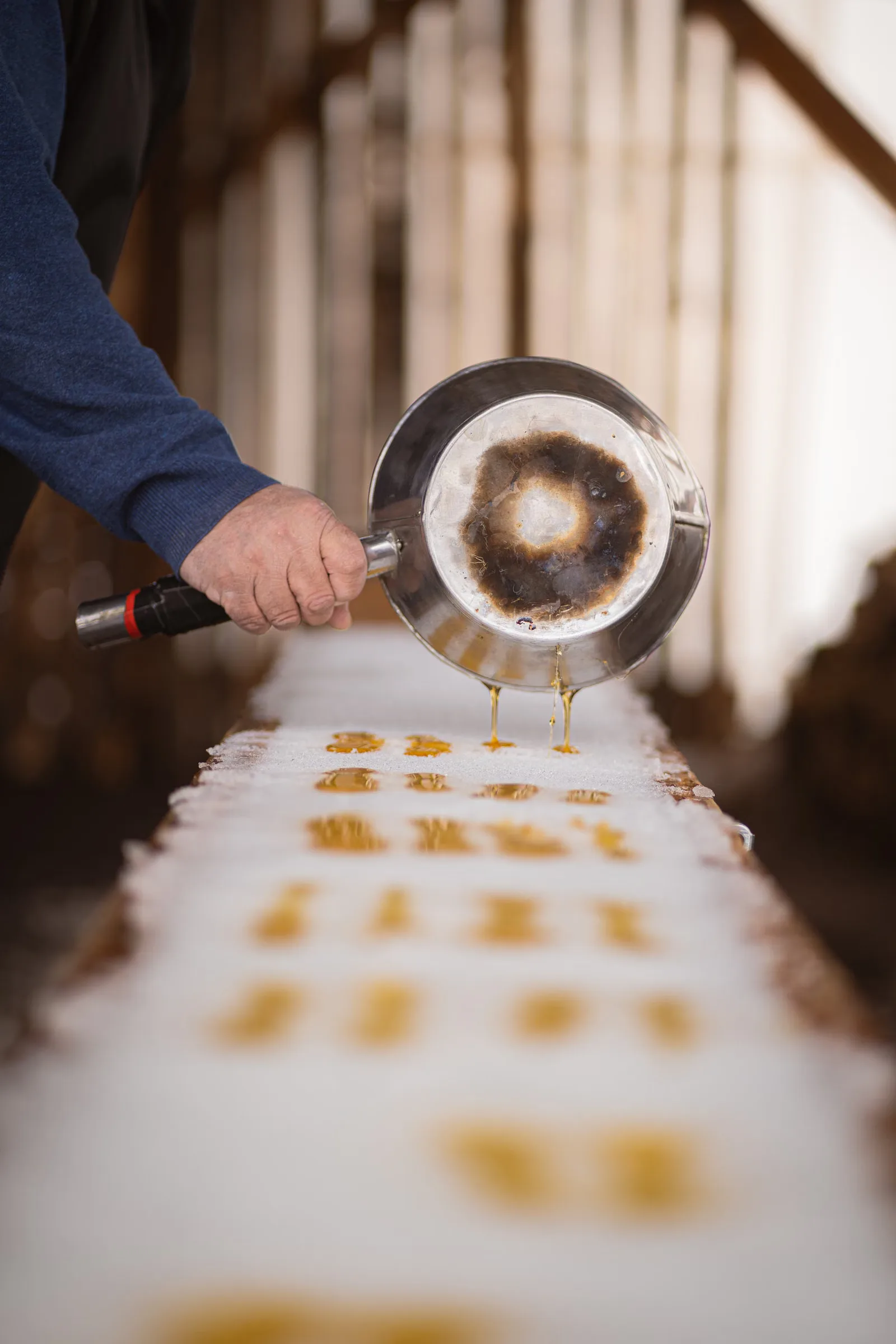 Main versant du sirop d'érable sur la neige au Québec, mettant en avant la fabrication traditionnelle de bonbons.