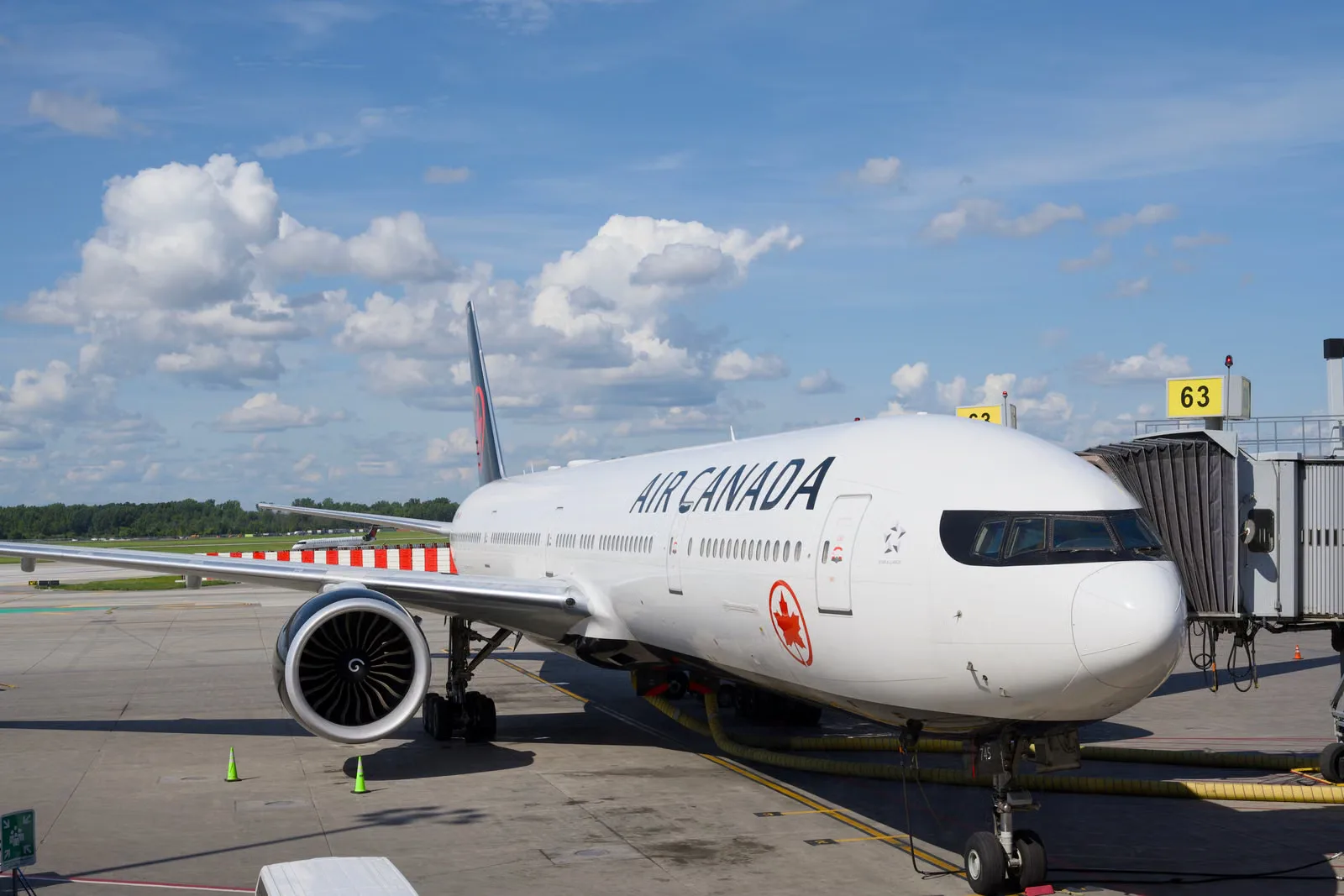 Un Boeing 777 d'Air Canada stationné à une porte d'embarquement sous un ciel bleu dégagé.