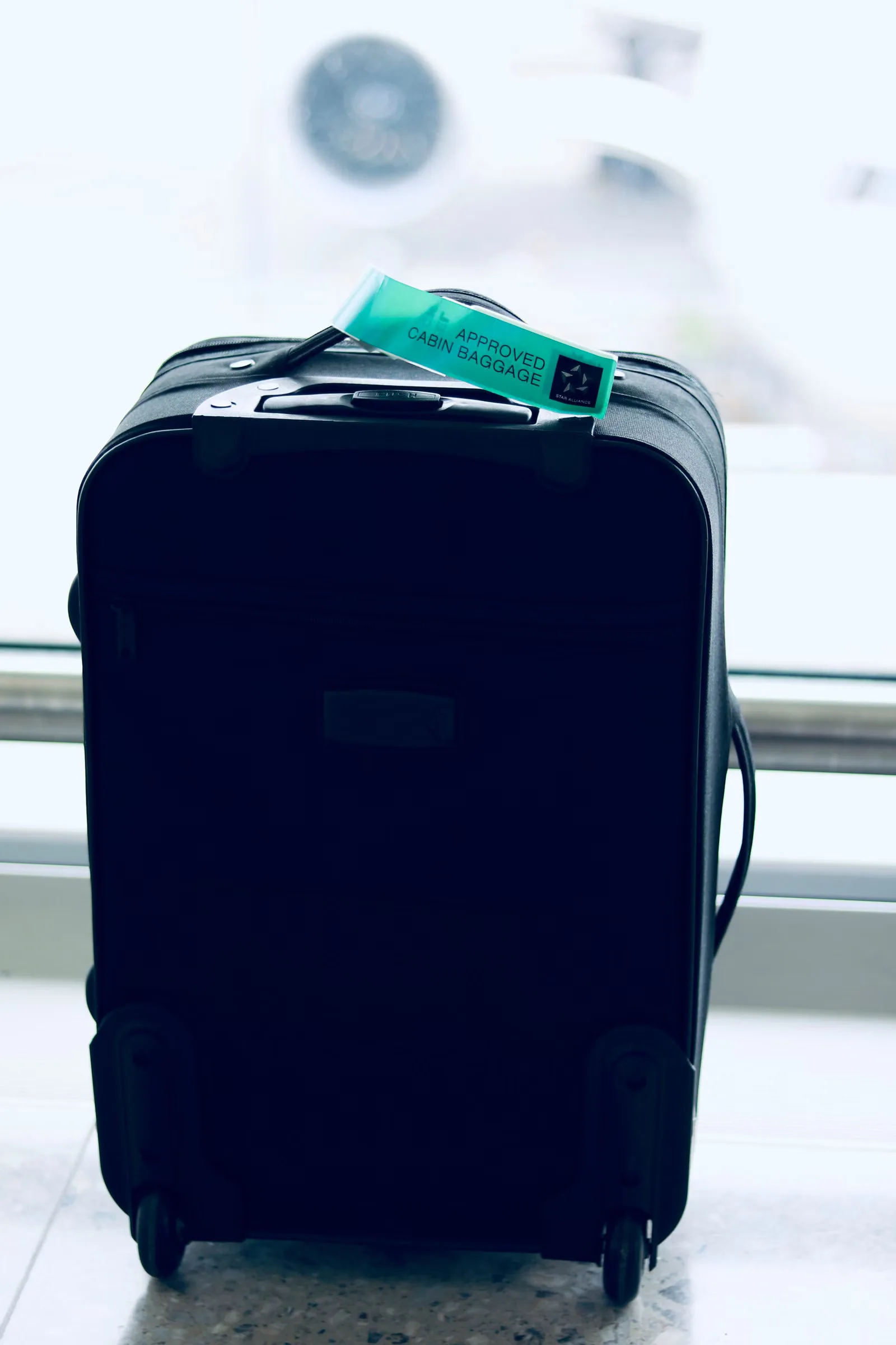 Gros plan sur une valise noire avec une étiquette approuvée pour cabine dans un cadre d'aéroport.