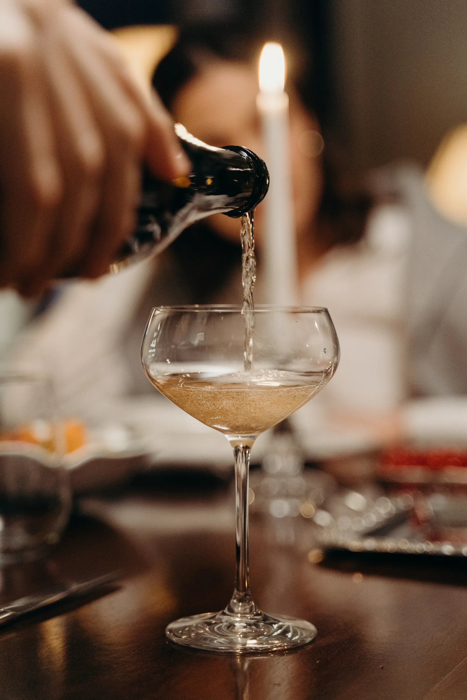 Gros plan sur du champagne versé dans une coupe, dans un décor de dîner aux chandelles.