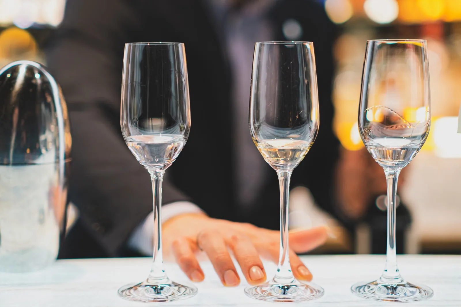 Une main de barman arrangeant des verres à vin vides sur un comptoir de bar, se préparant pour le service dans un bar parisien.