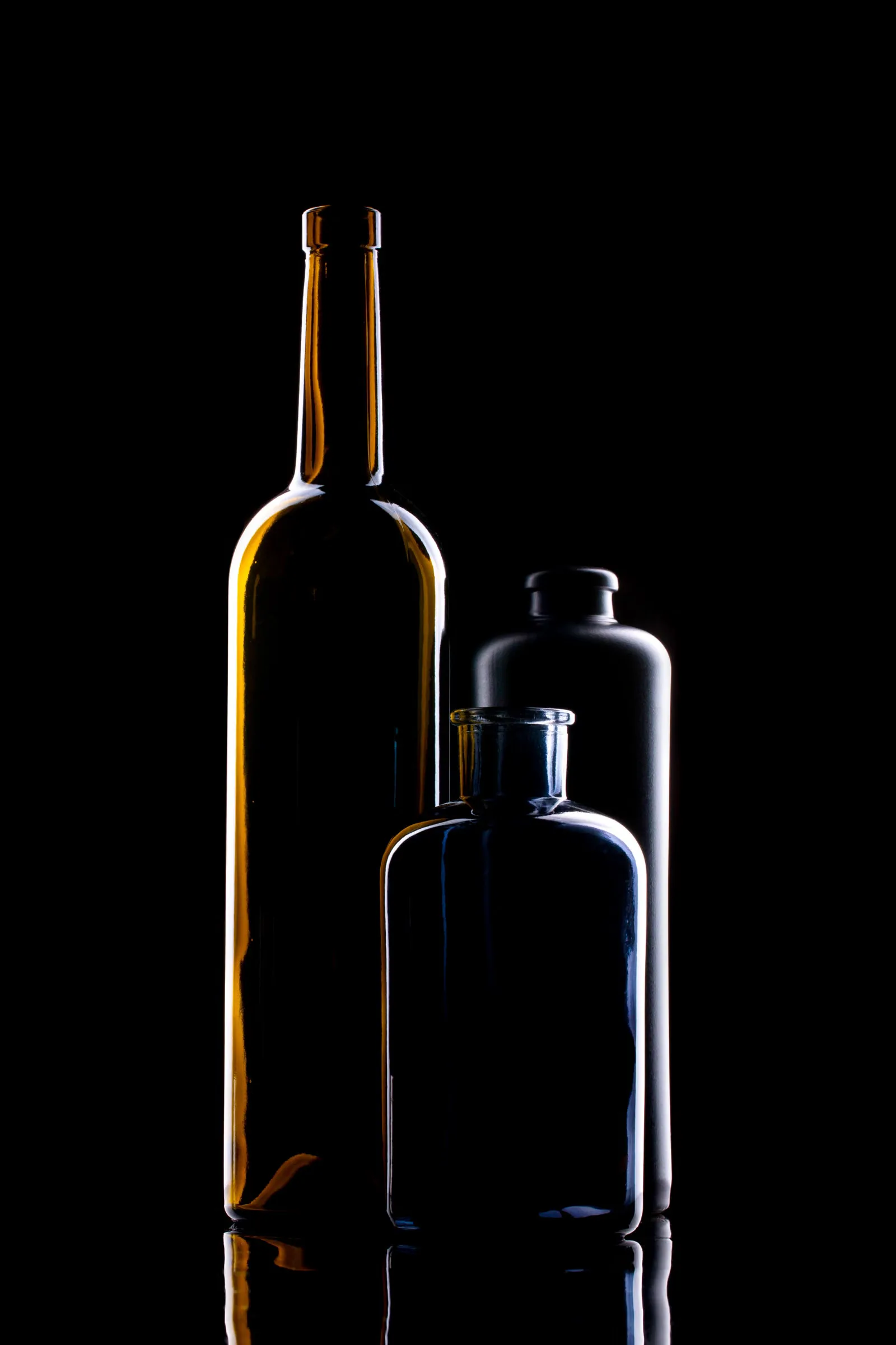 Arrangement élégant de bouteilles en verre colorées avec un éclairage dramatique sur un fond noir.