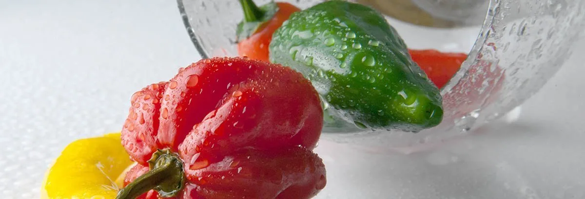 Une sélection de piments déboulant d'un bol transparent sur une table blanche