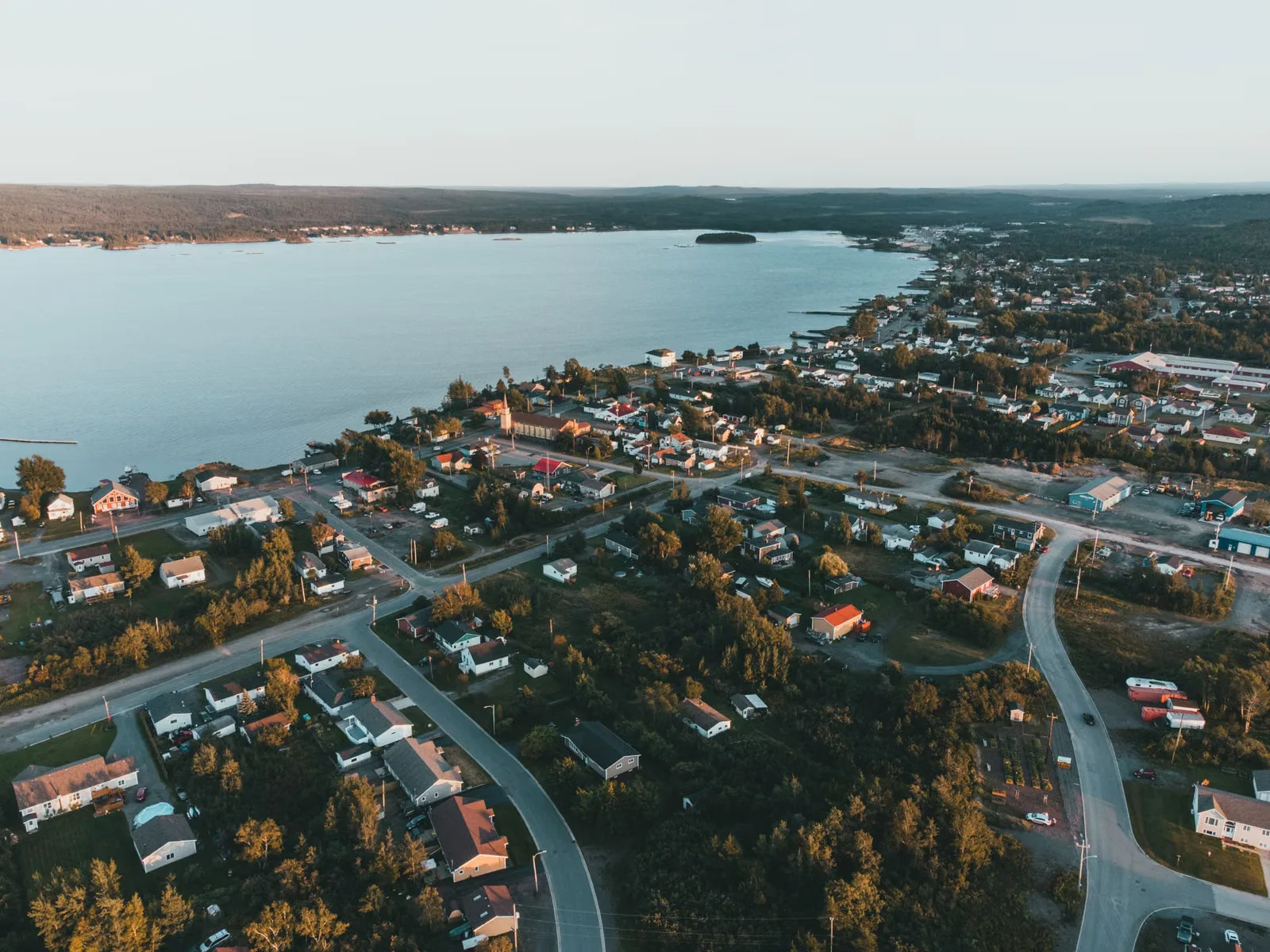 Vue aérienne d'un quartier résidentiel paisible au bord du lac avec des maisons et des routes pendant la journée.