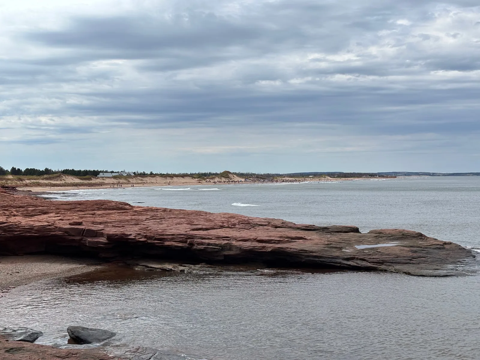 Magnifique vue côtière de la plage de Cavendish, Île-du-Prince-Édouard, avec un rivage rocailleux et un ciel nuageux.