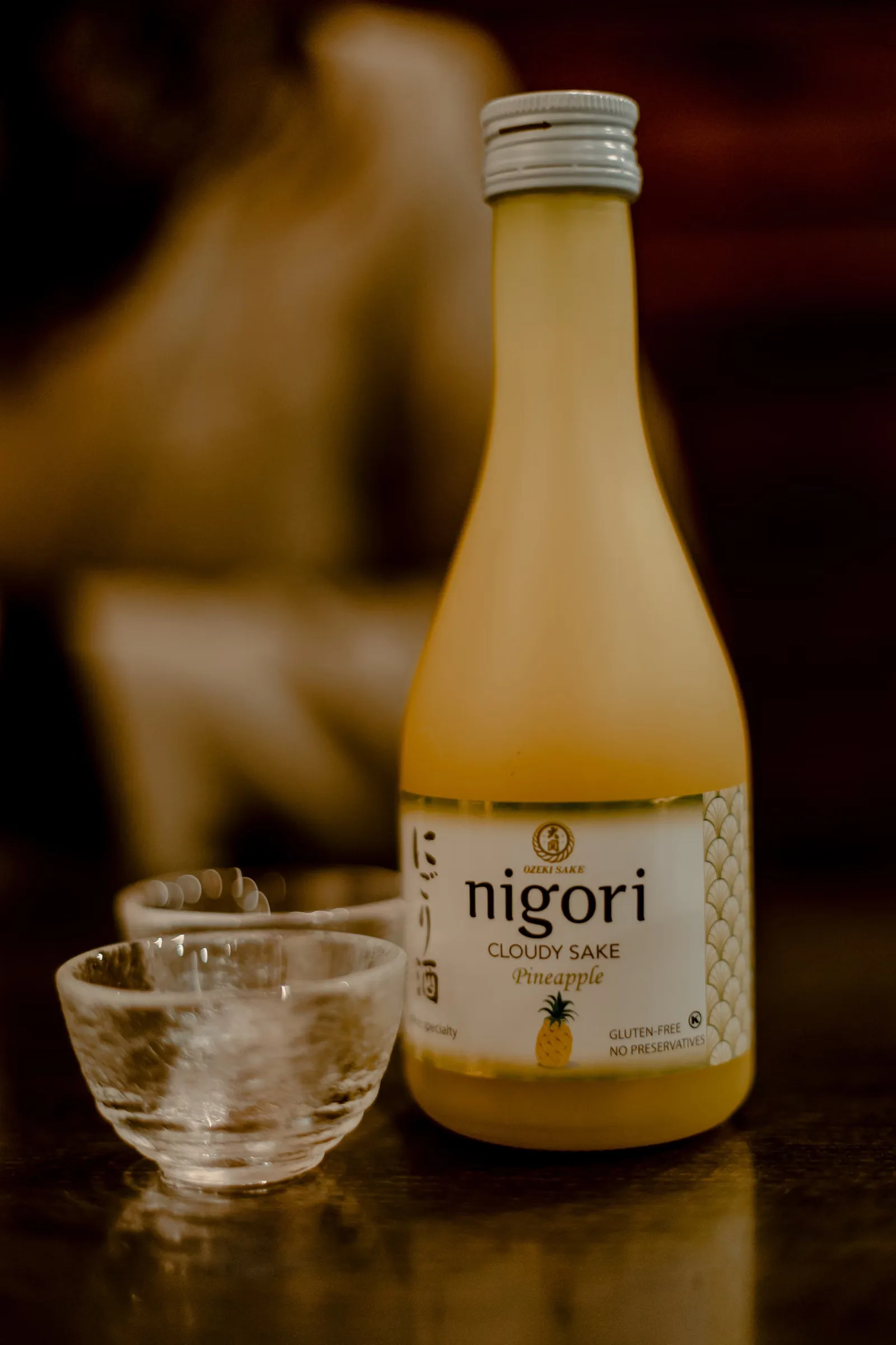 Une bouteille de saké nigori à l'ananas servie avec des verres à saké sur une table en bois.